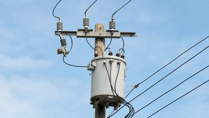 Cylindrical single-phase telephone pole transformer mounted on an overhead wooden utility pole with line cutouts