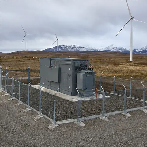 Completed and fenced prefabricated substation on a wind farm site with turbines in the background